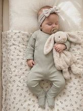 Load image into Gallery viewer, Baby wearing a sage green organic ribbed footed sleepsuit made from 95% organic cotton while sleeping with a soft bunny comforter.