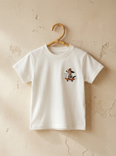Load image into Gallery viewer, White t-shirt with embroidered skateboarding dog graphic on beige background