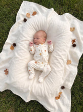 Load image into Gallery viewer, Newborn baby wearing a cream mushroom print organic cotton zip sleeper, sleeping on a white muslin blanket outdoors with autumn leaves and pine cones.