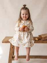 Load image into Gallery viewer, Toddler wearing the Croissant Print Organic Cotton Dress in cream with a rounded collar and gathered skirt.