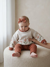 Load image into Gallery viewer, Baby wearing the oversized organic cotton Tulip Knit Jumper with soft pink tulip design in a warm neutral nursery setting.