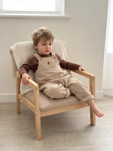 Load image into Gallery viewer,     Toddler boy wearing beige corduroy acorn dungarees with a brown long sleeve top, seated on a wooden chair.
