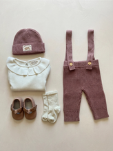 Load image into Gallery viewer, Dusty Pink Knit Braces Trousers styled with an ivory ruffle collar baby top, matching knit beanie, leather baby shoes and cream socks on a neutral background.
