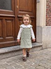 Load image into Gallery viewer, Toddler walking outdoors in a sage green corduroy pinafore dress and white long-sleeve blouse.
