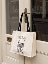 Load image into Gallery viewer, Ada Baby Bury St Edmunds reusable tote bag with black handles hanging from a shop door.
