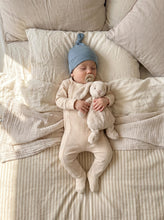 Load image into Gallery viewer, Baby wearing a cream organic ribbed footed sleepsuit made from 95% organic cotton while sleeping with a soft bunny comforter.
