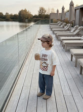 Load image into Gallery viewer, Child wearing organic cotton Babyccino graphic t-shirt while holding takeaway coffee cup beside lakeside deck
