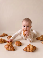 Load image into Gallery viewer, Baby wearing a cream organic cotton croissant print sleepsuit in a bakery-inspired setting
