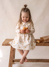 Load image into Gallery viewer, Toddler wearing a cream organic cotton dress with croissant print, rounded collar and long sleeves.
