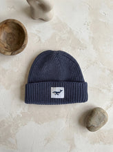 Load image into Gallery viewer, Dusty blue cotton knit beanie hat with whale patch for babies and children, photographed on a neutral textured background.
