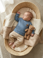 Load image into Gallery viewer, Baby wearing dusty blue long sleeve top with embroidered French bulldog detail while lying in Moses basket with teddy bear
