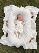 Load image into Gallery viewer, Newborn baby wearing an organic cotton mushroom print footed zip sleeper on a soft white muslin blanket in an autumn outdoor setting.
