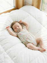 Load image into Gallery viewer, Baby wearing sea shell print muslin romper lying on white bedding
