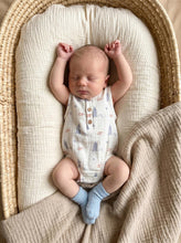 Load image into Gallery viewer, Baby wearing white organic cotton surf muslin romper lying on woven bassinet
